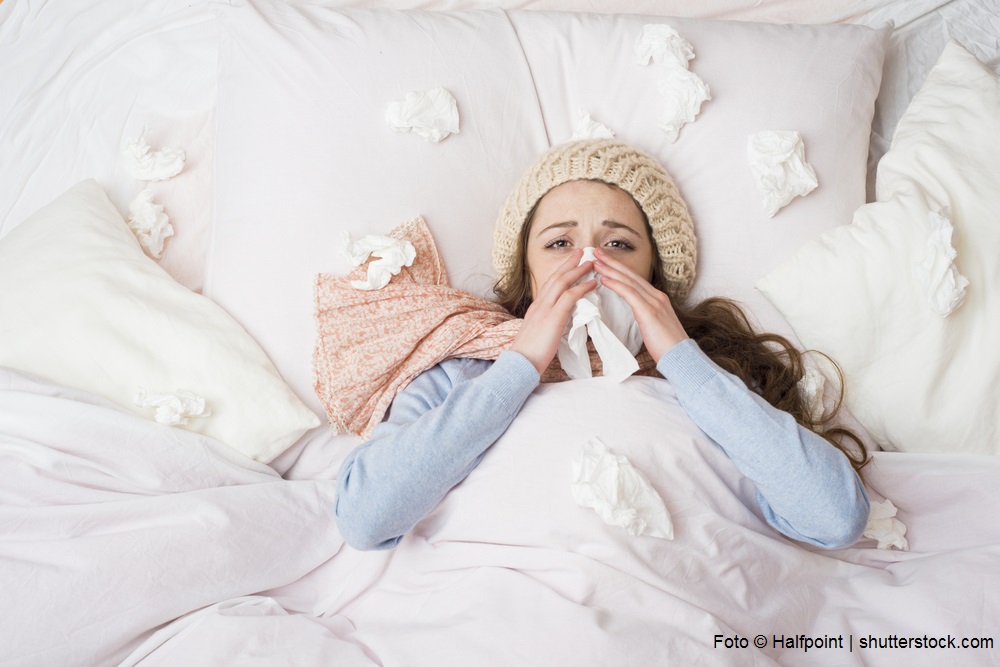 Frau liegt krank im Bett mit vielen Taschentüchern